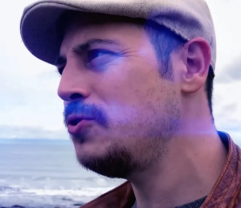 Shem Booth-Spain by the sea, in a flat cap, looking out to the left.